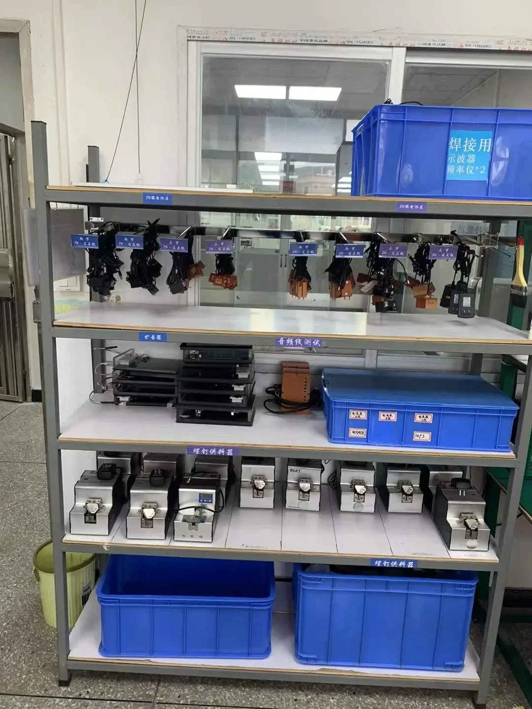Labeled storage positions for tools and test equipment, with blue containers on a workshop rack