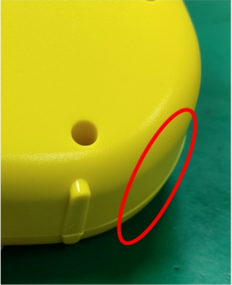 A red oval marks a surface step along the side joint of a yellow plastic housing.